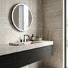 Round illuminated mirror with sleek black frame and soft LED lighting displayed on alabastrino rustic white vein-cut travertine tile