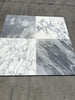 Four marble-like square tiles featuring Arabescato Corchia patterns in white and gray finishes