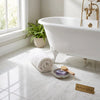 White rolled towel on polished bianco dolomite 12x12 marble floor beside a classic clawfoot tub