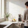 Black and silver electric coffee grinder with transparent hopper and container with Bianco Dolomite 12x24 marble tile background