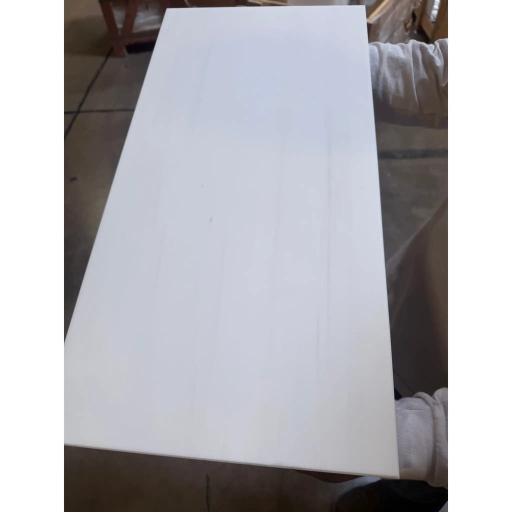 A person holding a smooth glossy white rectangular Bianco Dolomite marble panel polished or honed 12x24 inches