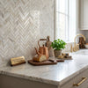 A polished copper teapot with wooden handle on calacatta gold 1x4 herringbone mosaic marble tile countertop
