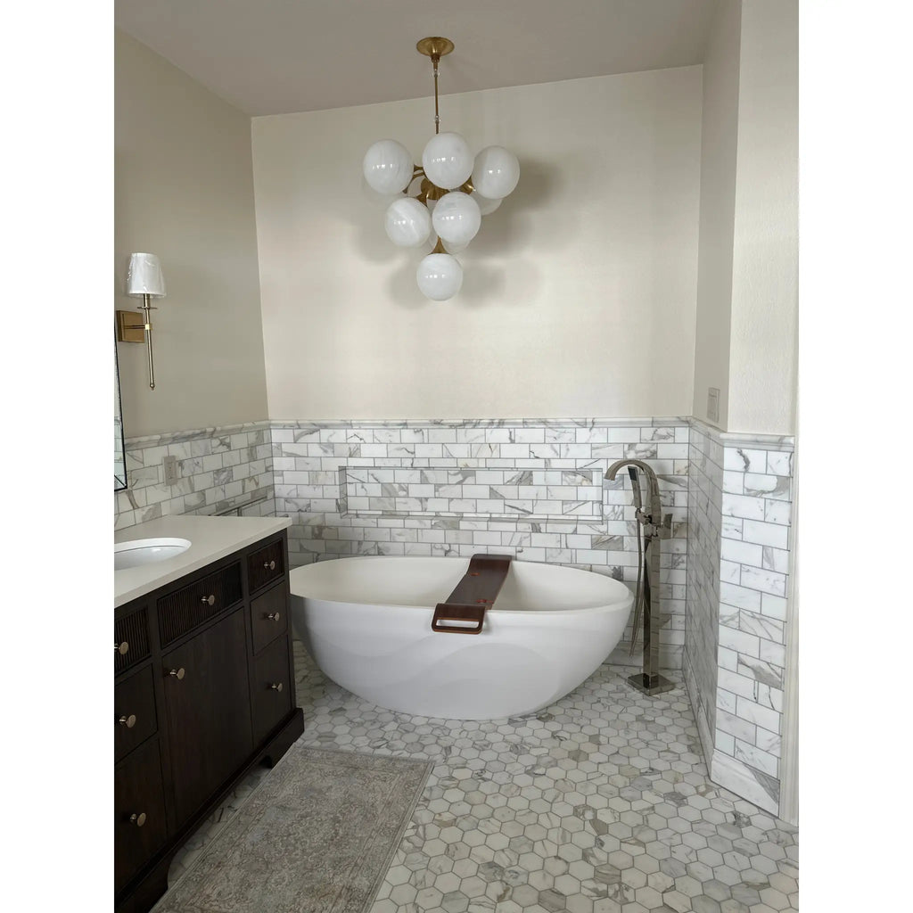 White freestanding bathtub with brown wooden bath mat featuring calacatta gold 2 inch hexagon mosaic marble tile