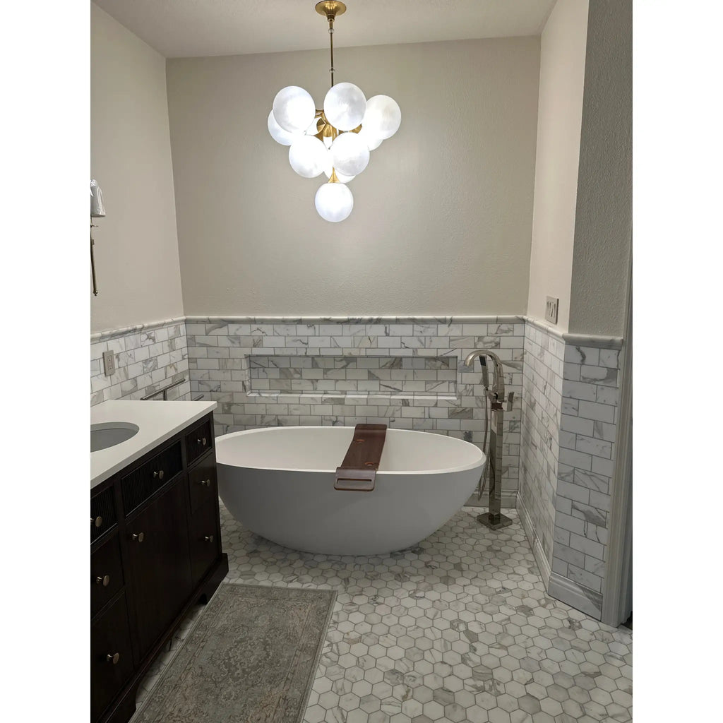 White oval freestanding bathtub with brown towel on calacatta gold 2 inch hexagon mosaic marble tile polished or honed