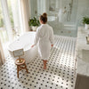 White bathrobe with belt and long sleeves displayed alongside polished calacatta gold basketweave mosaic marble tile