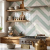 Gold-colored brass teapot with wooden handle and lid knob displayed alongside Calacatta Gold Chevron mosaic marble tile