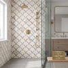 Gold-toned showerhead with modern design on brass shower system set against calacatta gold fan raindrop mosaic marble tile