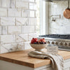A ceramic bowl with speckled beige glaze filled with pomegranates and figs displayed on calacatta gold marble tile