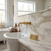 Gold-finished faucet with white ceramic handles mounted on calacatta gold marble 6x12 polished wall