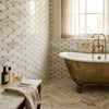 Antique brass clawfoot bathtub with white porcelain interior and ornate feet beside calacatta gold octave mosaic marble tile
