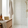 Beige towel with embroidered monogram hanging by window next to polished calacatta gold pinwheel mosaic marble tile