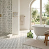 White clawfoot bathtub with elegant curved legs beside calacatta gold triple-weave ming-green polished marble tile