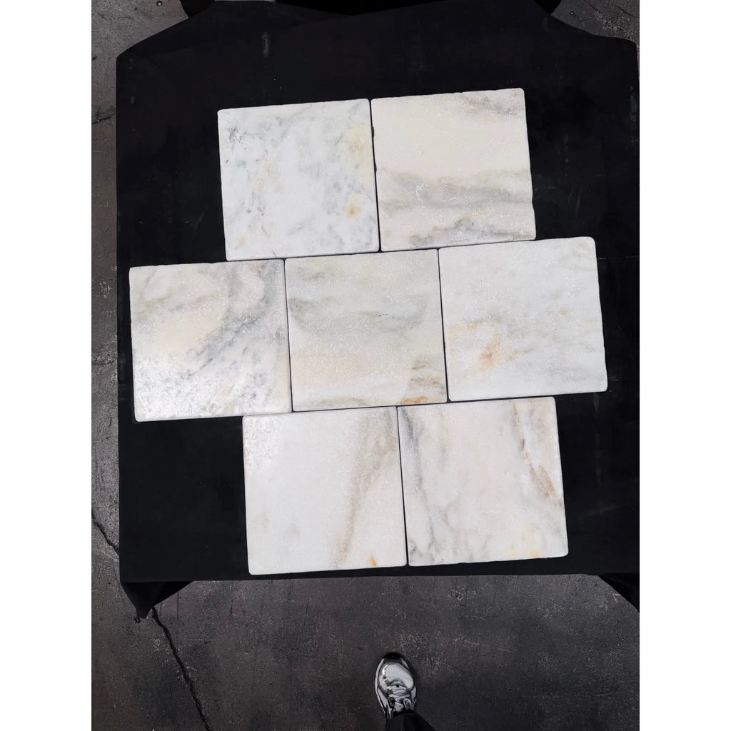 Six square white calacatta verde royale marble 12x12 tiles with subtle gray veining arranged in a cross pattern on black surface