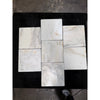 White marble 12x12 tiles with subtle gray and beige veining arranged in a cross pattern on a dark surface