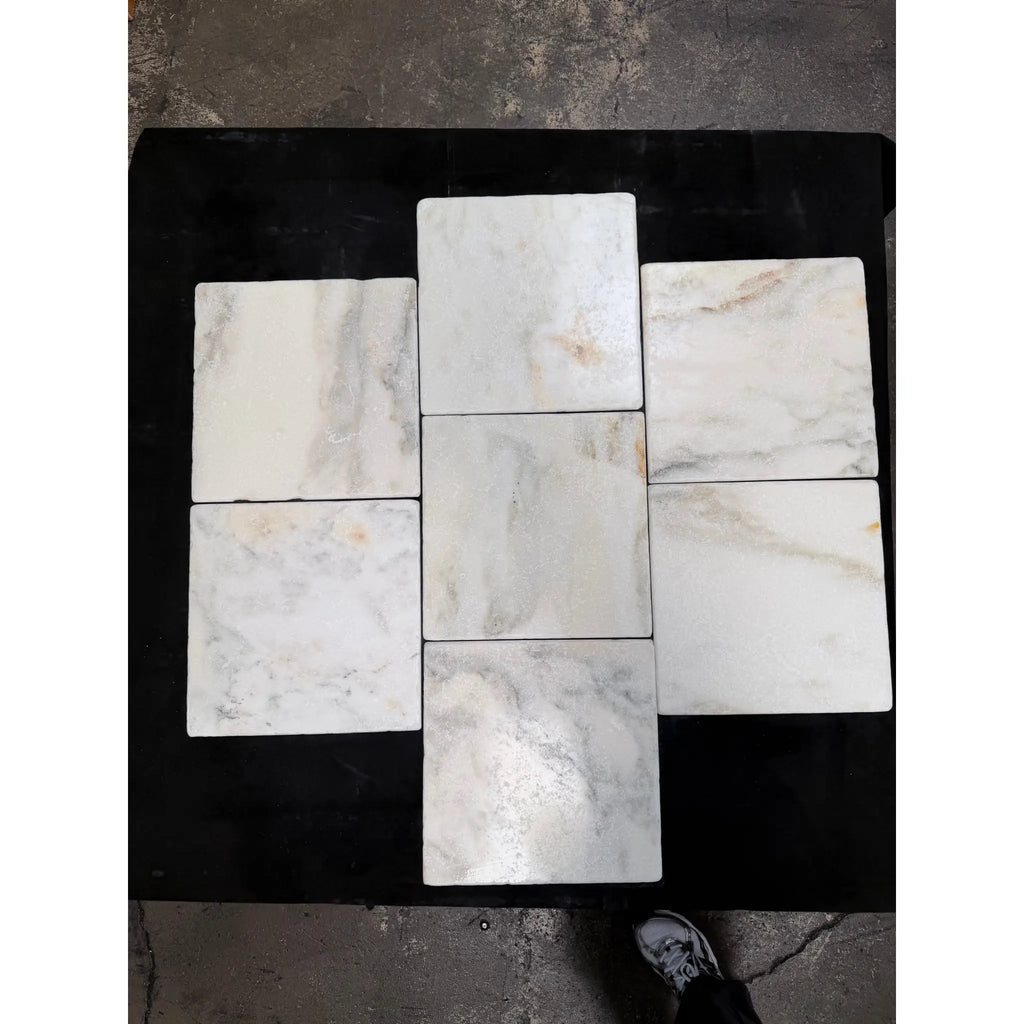 White marble 12x12 tiles with subtle gray and beige veining arranged in a cross pattern on a dark surface
