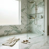 A modern showerhead with a sleek brushed metallic finish and curved design complements calacatta verde royale marble tile