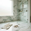 A modern showerhead with a sleek brushed brass finish and adjustable hose paired with calacatta verde royale marble 12x24 tile polished or honed
