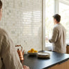 A copper teapot with wooden handle and lid on a dark countertop featuring Calacatta Verde Royale marble 1x1 mosaic tile