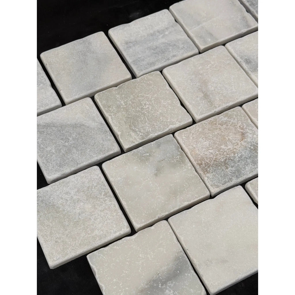 Square light gray calacatta verde royale marble 4x4 tumbled tile with subtle veining and a slightly rough texture