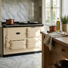 Cream-colored aga range cooker with black enamel top and classic panel design shown with calacatta verde royale marble tile