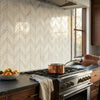 A copper pot with a long handle on a stovetop featuring calacatta verde royale marble chevron mosaic tile polished