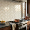 A copper pot with a long handle on a stovetop next to polished calacatta verde royale marble chevron mosaic tile