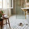 White towel rolled neatly on wooden stool beside polished calacatta verde royale marble octave with black mosaic tile