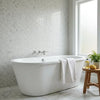 White freestanding bathtub with sleek oval shape and chrome fixtures shown with calacatta verde royale marble penny round mosaic tile