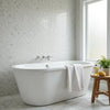 White freestanding bathtub with a sleek oval shape and smooth porcelain finish paired with calacatta verde royale marble penny round mosaic tile polished