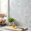 A copper kettle with rounded handle and spout on a stovetop with polished carrara white 2x4 brick mosaic marble tile background