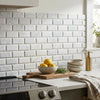 A ceramic bowl with bright yellow lemons on a rustic wooden board beside polished honed carrara white 2x4 marble tile mosaic