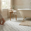 Cream-colored clawfoot bathtub with polished chrome faucet beside carrara white florida flower mosaic marble tile panel