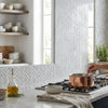 A copper pot with stainless steel handle on stovetop next to polished carrara white herringbone mini marble tile mosaic
