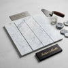 Four rectangular carrara white marble 3 x 12 field tiles with subtle gray veining arranged neatly on a light surface
