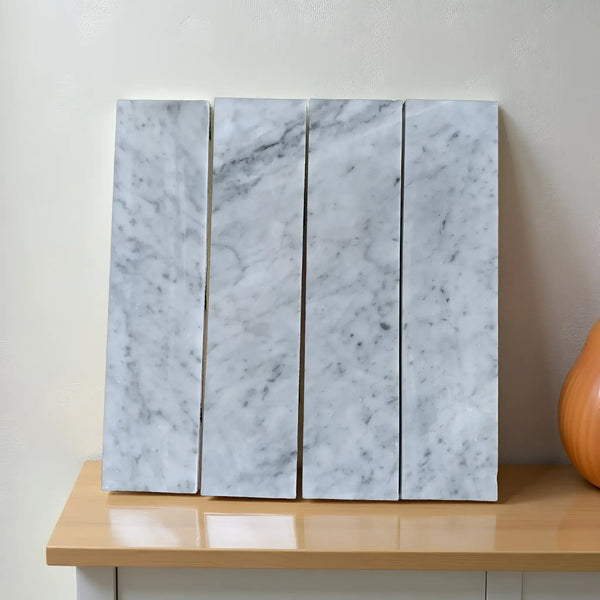 Four Carrara White Marble 3’’ X 12’’ Field Tiles arranged on a neutral surface