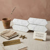 White italian carrara marble hexagonal tiles with subtle gray veining in 3 by 12 inch picket mosaic pattern