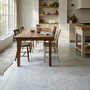 Rustic wooden dining table with natural finish and visible grain surrounded by matching chairs with carrara white marble tiles