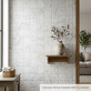 A textured off-white ceramic vase with subtle gray veining on a wooden shelf showcasing Carrara white marble 6x6 tumbled tile