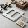 Carrara white marble double rocker switch wall plate with subtle veining and gold-colored metal accents