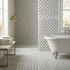 White clawfoot bathtub with ornate silver feet next to polished carrara white stanza black mosaic marble tile