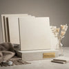 Cream-colored textured concrete Champagne Lymra 24x24 limestone honed tile sample on matching pedestal with gold plaque