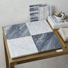 Gray and white marble tile samples arranged in a four-square grid on a gold table for checkerboard bardiglio and bianco carrara set