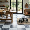A black and white speckled dog resting on a woven jute rug with checkerboard bardiglio nuvolato and oriental white tiles
