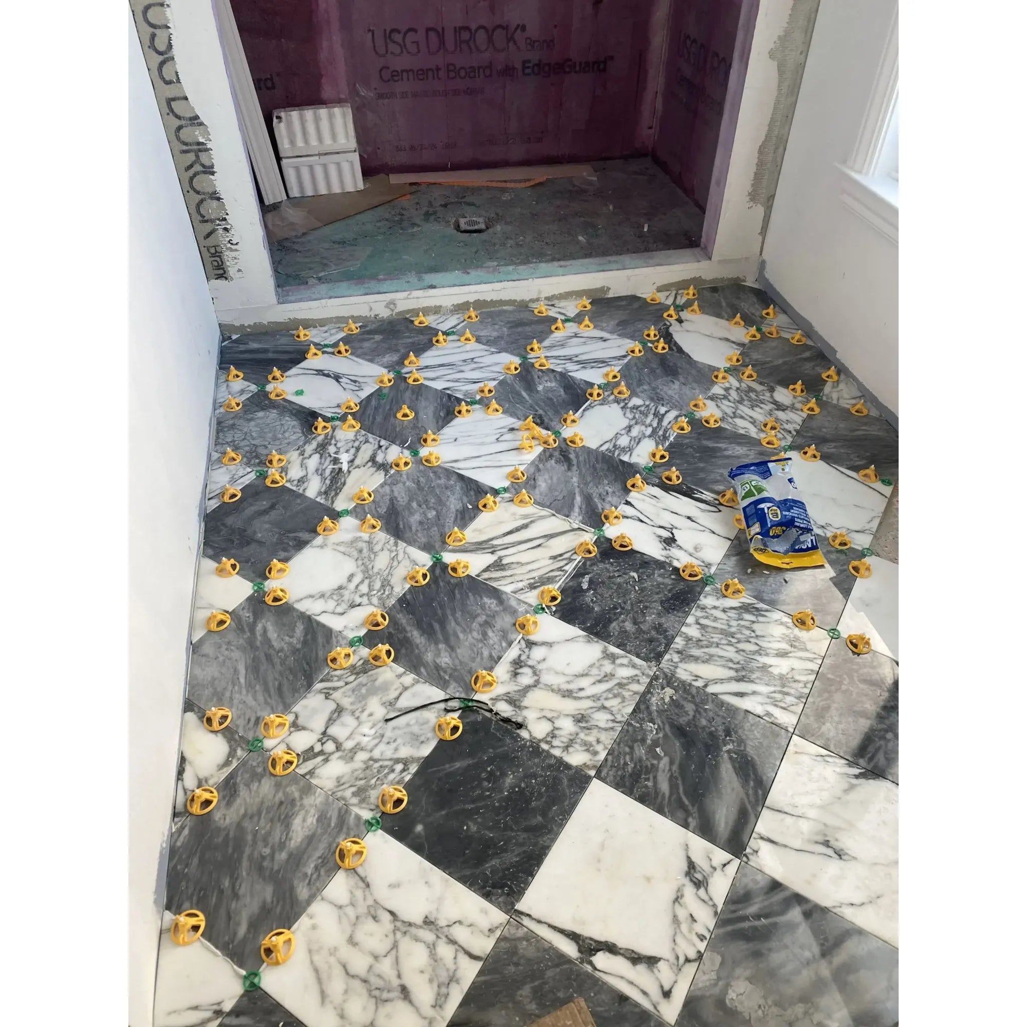 Marble tile floor featuring yellow spacers in Checkerboard Nero Marquina and Arabescato Corchia set