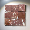 Nine square tiles of Crema Marfil tumbled marble with reddish-brown color and veining