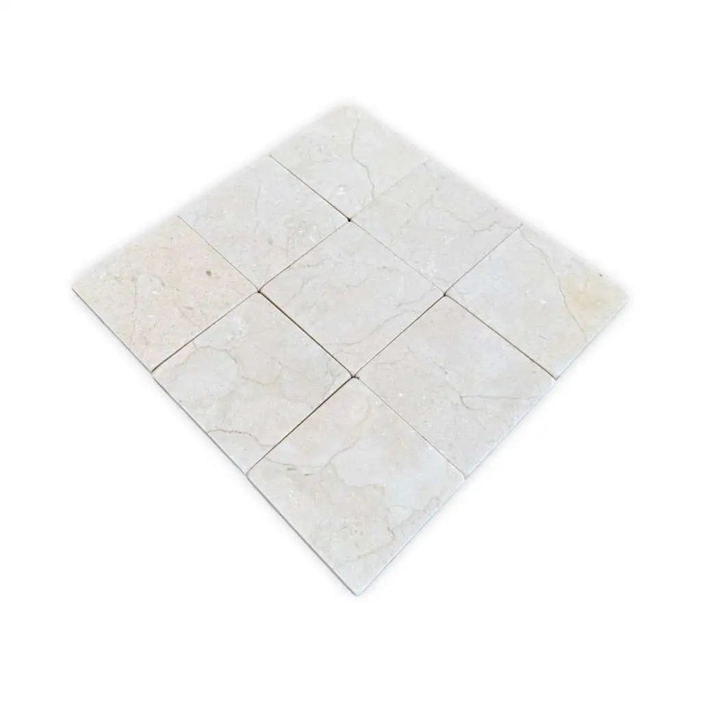 A grid of twelve light-colored Crema Marfil 4X4 Tumbled natural stone tiles with subtle variations