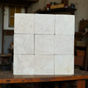 Stack of nine light-colored Crema Marfil 4X4 Tumbled stone tiles with natural veining