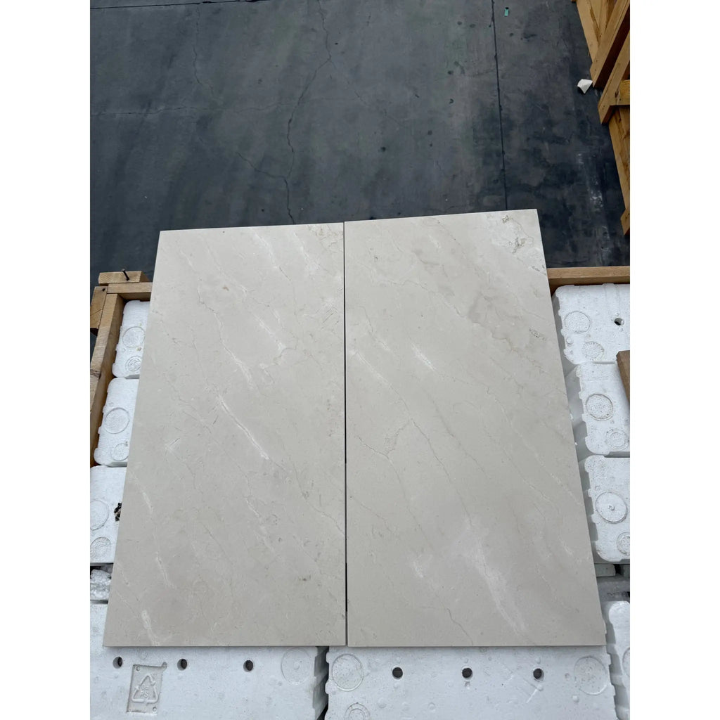 Two rectangular light-colored Crema Marfil marble tiles showcasing polished or honed finish