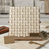 Cream-colored crema marfil marble tile sample with three-dimensional woven grid pattern and brass hardware