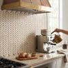 Brass kettle with wooden handle pouring into white cup on polished crema marfil marble chevron mini mosaic surface
